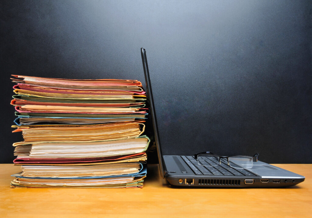 Stack of folders next to an open laptop on a wooden desk.
